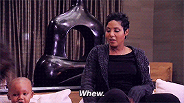 Toni Braxton saying 'whew' and sliding into her chair next to a baby